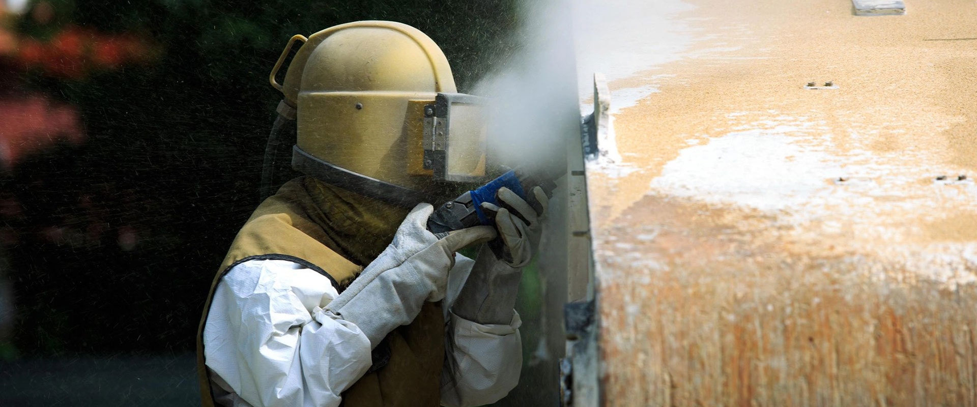 Technician in full protective helmet and gear soda blasting a surface